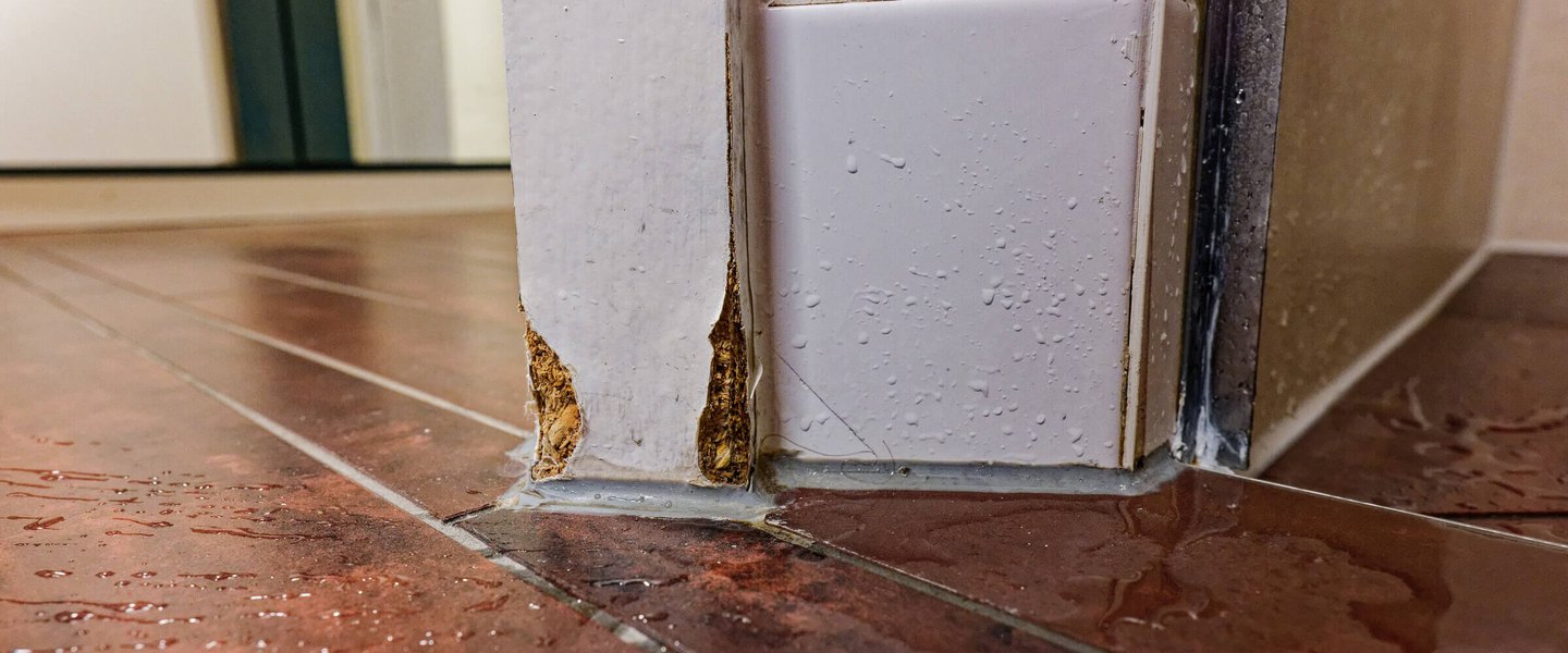 Water Intrusion and Moisture Water on a tile floor with a swollen door panel from moisture intrusion